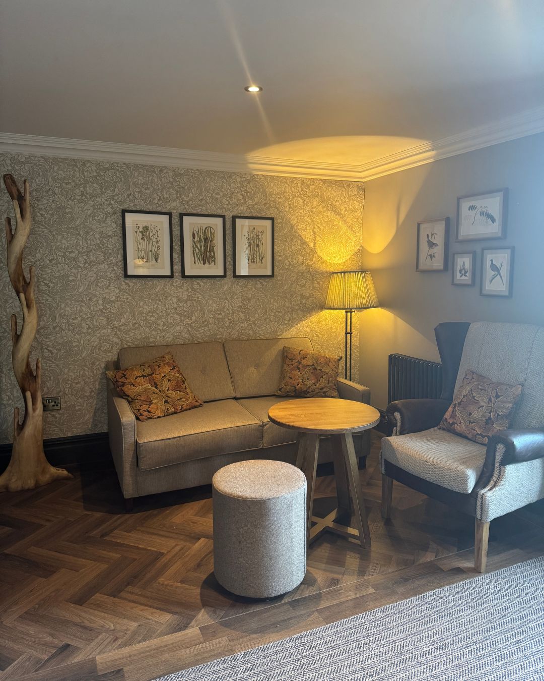 A cosy corner of a bedroom with a sofa, armchair and a coffee table, warmly lit by a lamp in the corner.
