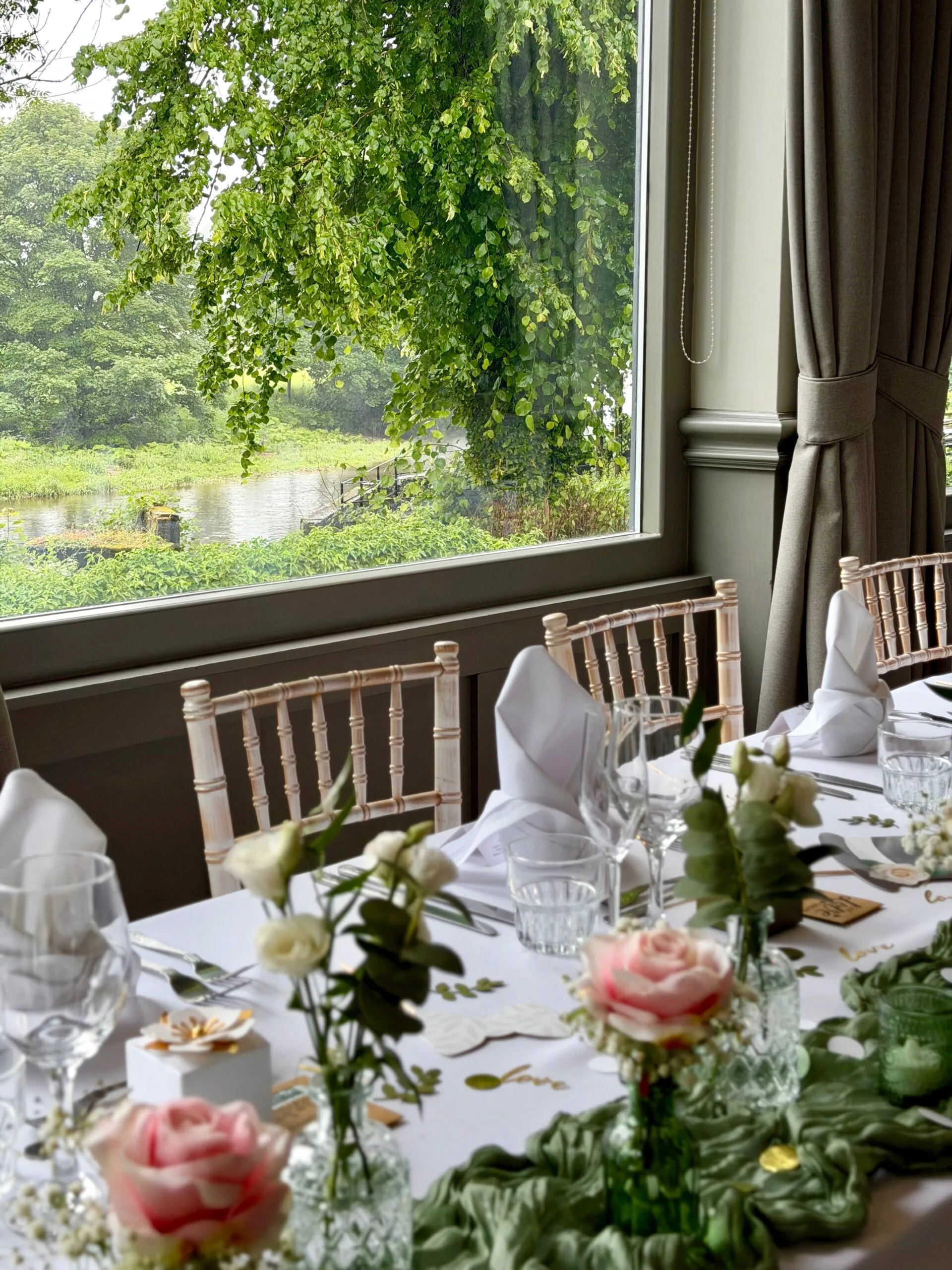 A wedding breakfast table at the Spread Eagle set with crisp white linen, sage green cheesecloth runners and small glass bud vases of white roses, pink blooms, gypsophila and eucalyptus.
